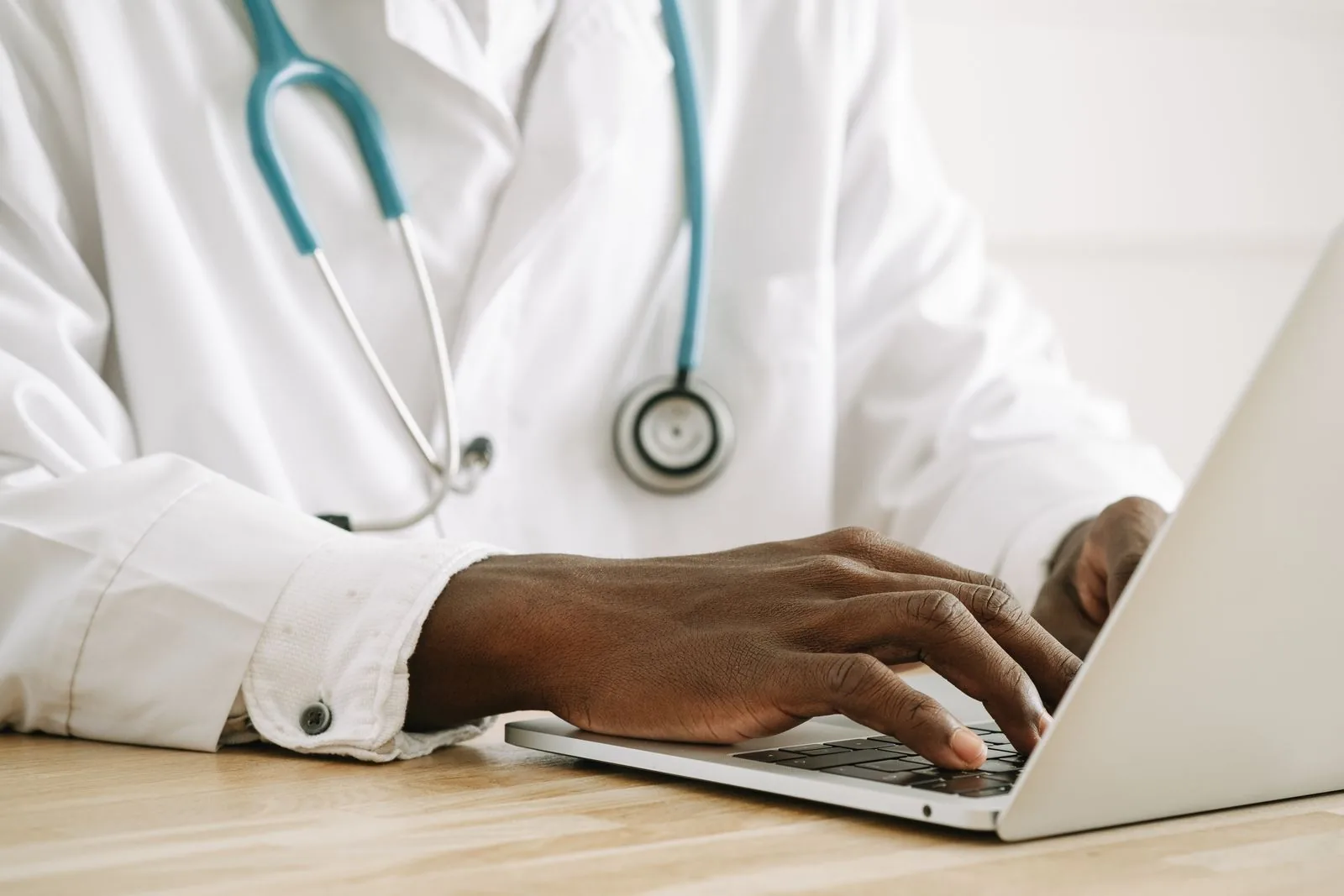 Primo piano di un medico che utilizza un laptop, indossando uno stetoscopio e un camice bianco.